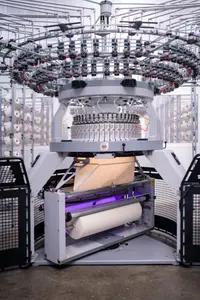 A modern industrial knitting machine with hundreds of yarn cones in the background
